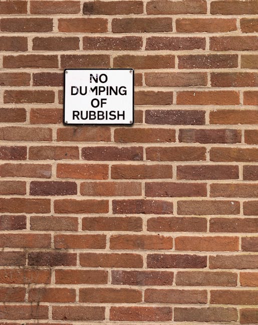 A close-up view of a brick wall with a rectangular metal sign mounted in the upper left section. The sign has a white background with black text that reads 'NO DUMPING OF RUBBISH', although part of th